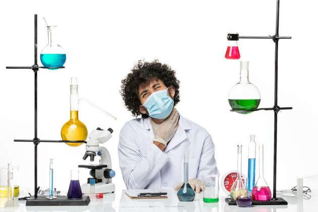 坐着正面图：男化学家 穿着医疗服 戴着面罩 坐在白色的空间里溶液病毒实验室外套