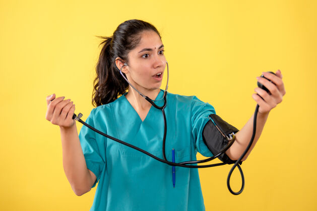 护士正面图身着制服的美丽女医生手持血压计站在黄色背景上医疗器械医院医生