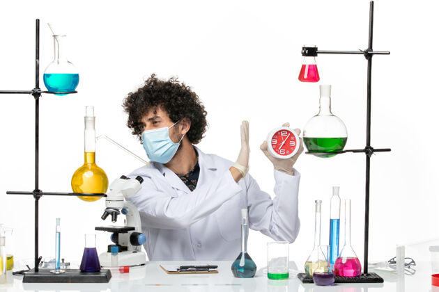 外套前视图男性化学家穿着医疗服 戴着面罩 在浅白色的空间里拿着时钟正面专业面具
