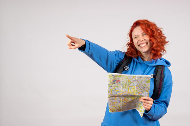 微笑年轻女性的正面图 白色墙上有背包和地图旅行成人假期