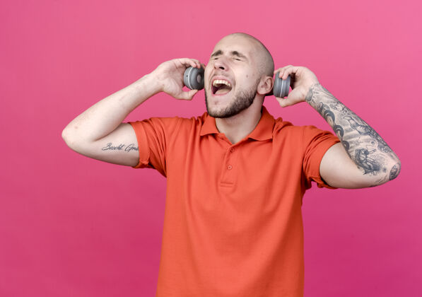 周围闭上眼睛 快乐的年轻人 戴着耳机 耳朵被隔离在粉红色的墙上封闭耳机年轻