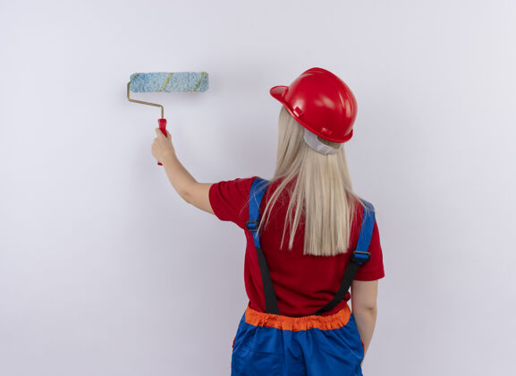 立场年轻的金发工程师建筑女孩在统一的油漆墙油漆辊站在后面的看法孤立的白色墙壁女人油漆金发