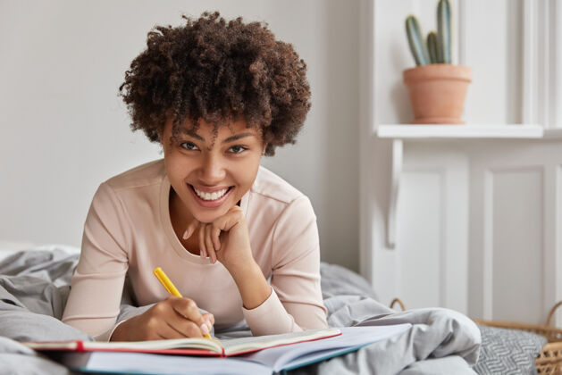 记者快乐的年轻美国黑人女士用钢笔在笔记本上写下信息的照片表达现代日记