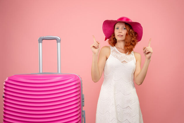 航行年轻的女性游客与粉红色的帽子和粉红色的墙壁上的包的正面视图前面美丽连衣裙