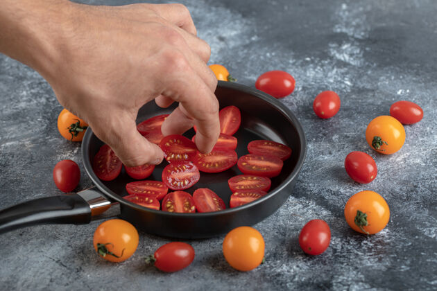 平板男人从煎锅里拿着切了一半的樱桃番茄食物手有机