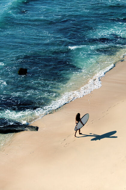 海洋美丽的女孩拿着冲浪板走在荒野的海滩上从山顶看风景很美景观人人