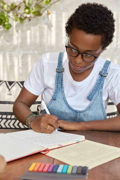 民族留着孩子气发型的黑人妇女 用笔在笔记本上写字 努力完成功课忙碌钢笔青少年