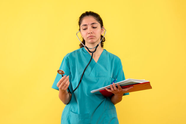 医院穿着制服的女医生正看着黄色墙上拿着纸的听诊器诊所医生药