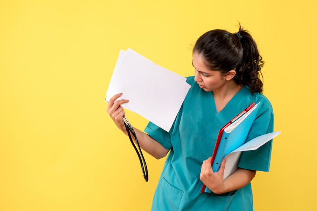听诊器站在黄色墙上的年轻女医生检查文件的正面图检查纸前面