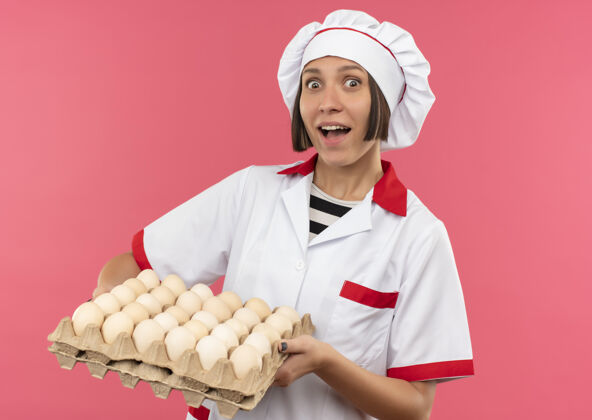 女年轻的女厨师穿着厨师制服 手里拿着一盒粉红色的鸡蛋纸箱持有制服