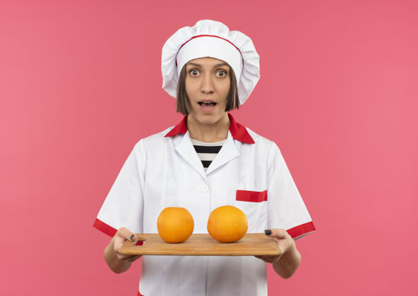 复制穿着厨师制服的年轻女厨师手拿着砧板 砧板上有橘子 粉红色 有复印空间橙色空间持有