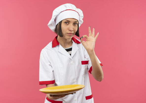 厨师自信的年轻女厨师 身着厨师制服 手拿空盘子 手拿ok标志 粉色 有复印空间年轻制服烹饪