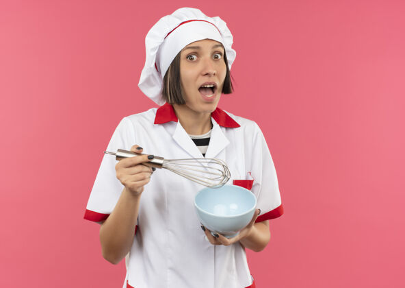 制服令人印象深刻的年轻女厨师在厨师制服举行威士忌和碗孤立的粉红色与复制空间年轻复制女