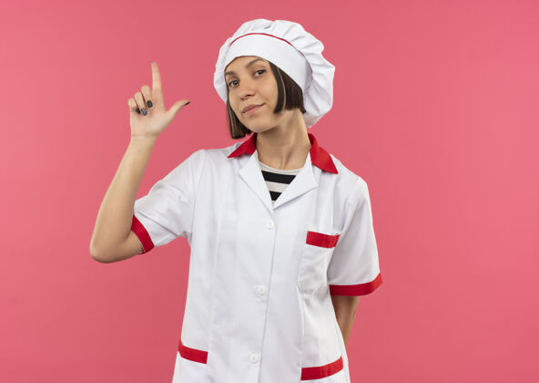 年轻自信的年轻女厨师身着厨师制服 做着式的手势 在粉色的地板上单独复制空间自信复制