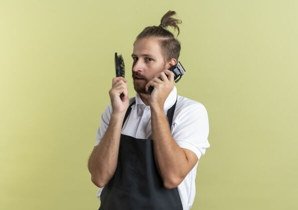 梳子自信的年轻英俊的理发师拿着梳子和理发器假装在讲电话用理发器作为电话隔离在橄榄绿与复制空间橄榄复制使用
