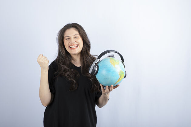 女人面带微笑的年轻女子戴着耳机站着拿着地球仪看全球地点