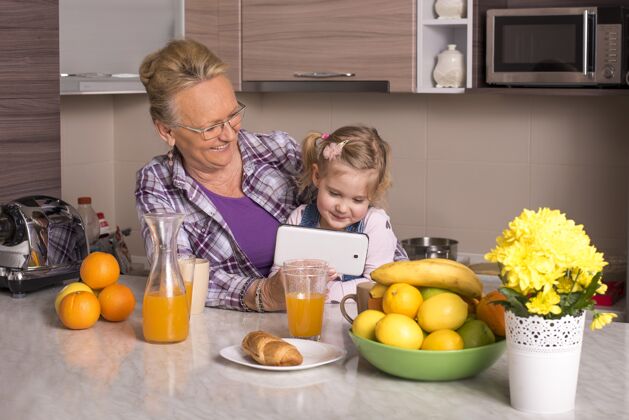 Pc一个祖母和她的孙子看智能手机的浅焦镜头烹饪室内女人