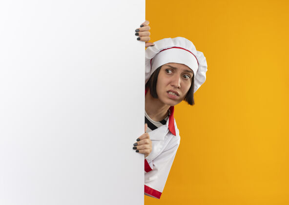 女性焦急的年轻女厨师身着厨师制服 从后面的白色墙壁上看一边隔离着橘黄色的空间烹饪墙壁橙色