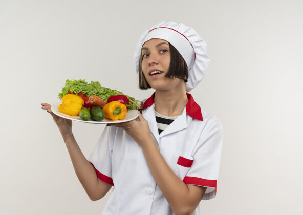 印象印象深刻的年轻女厨师在厨师制服举行的蔬菜盘上白色隔离与复制空间女蔬菜空间