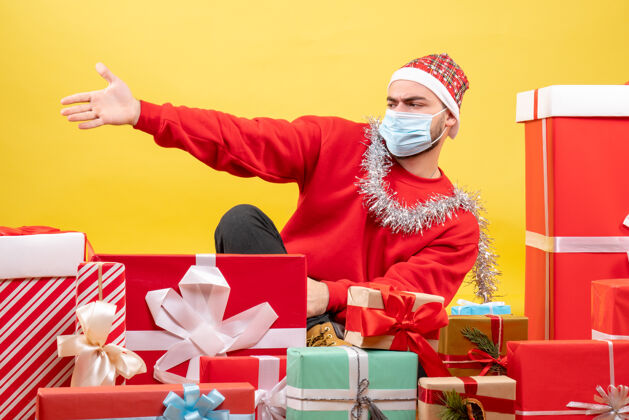 病毒正面图：坐在黄色背景上的年轻男性礼物帽子流行病圣诞节