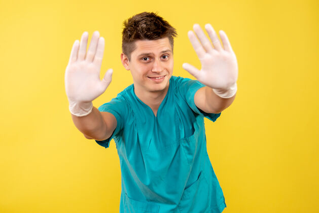 人正面图年轻的男医生穿着医疗服 戴着黄色背景的手套健康男人年轻男性医生