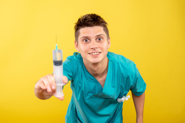 微笑正面图黄色背景上穿着医疗服拿着针剂的年轻男医生刷子年轻男性医生背景