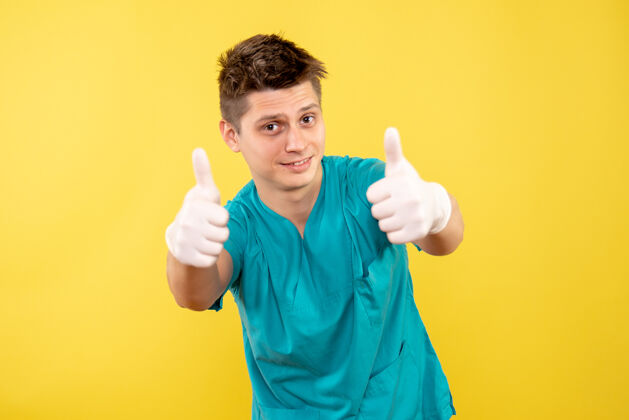 成人正面图：年轻的男医生穿着医疗服 戴着黄色背景的手套人医学套装