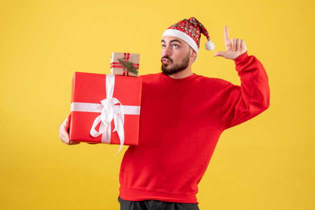 礼物黄色背景下手持圣诞礼物的年轻男性正面图年份人雪