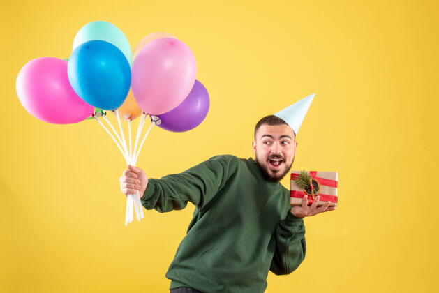 背景正面图：手持彩色气球的年轻男性 背景为黄色年礼物聚会