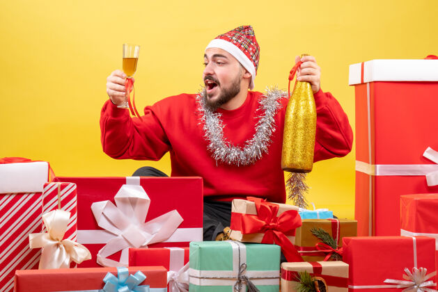坐着正面图年轻男性围坐在黄色背景上庆祝香槟庆祝圣诞节盒子