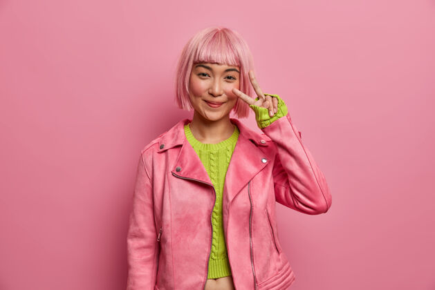 鲍勃快乐的亚洲女人展示v字 保持冷静和积极 穿着时尚的粉色夹克 绿色毛衣 享受胜利 积极的手势亚洲人粉色假发手指