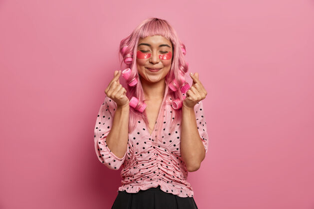 理发真诚积极的女人 长着粉红色的头发 涂上卷发 做卷发 显示韩国人的心迹 戴上玫瑰色的胶原蛋白贴片来减少浮肿情感垫流苏