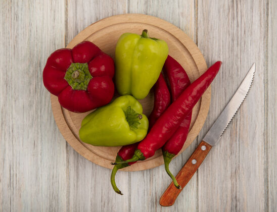观点顶视图新鲜的铃铛和辣椒在一个木制的厨房板上用刀在灰色的木墙上辛辣菜肴膳食