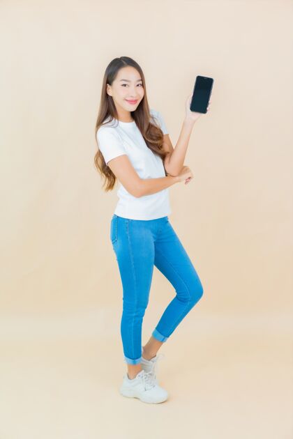 电话肖像美丽的亚洲年轻女子在米色上使用智能手机聪明漂亮女人