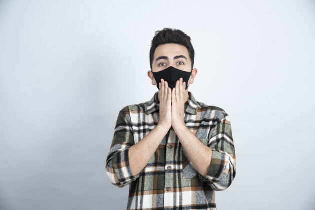 安全戴着黑色防冠状病毒面具的年轻人站在白墙上的照片疾病防护流感