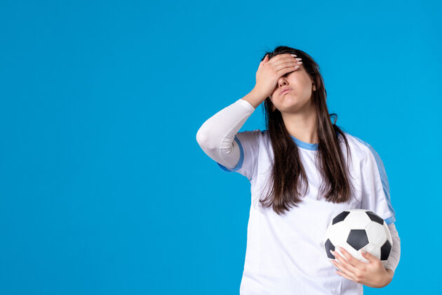 足球前视图：蓝色墙上有足球的年轻女性年轻人体育人物