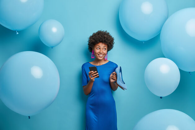 生日穿着蓝色裙子的美女 手拿高跟鞋 手拿手机 生日派对 被氦气球包围 为特殊场合选择服装 享受活动非洲微笑积极