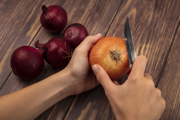 切割俯视图中的女性手切黄洋葱与红洋葱隔离在一个木制的墙壁刀食物女薯条