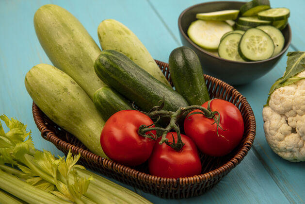 有机健康蔬菜的俯视图 如西红柿 黄瓜和西葫芦放在桶上 菜花和芹菜被隔离在蓝色的木墙上农场食品番茄