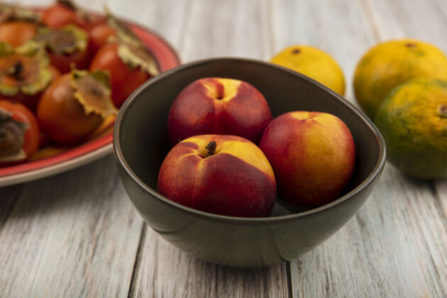 有机新鲜柔软的桃子放在碗里 橘子被隔离在灰色的木墙上饮食桃水果