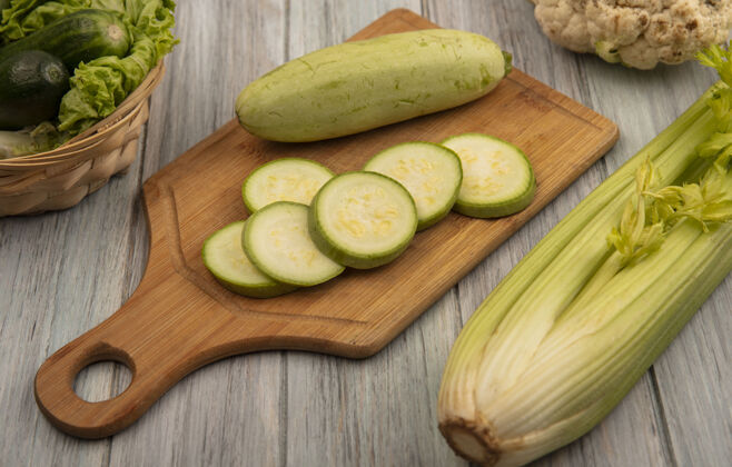 芹菜顶视图富含维生素的西葫芦放在木制厨房板上 黄瓜和生菜放在桶上 芹菜被隔离在灰色的木墙上观点新鲜厨房