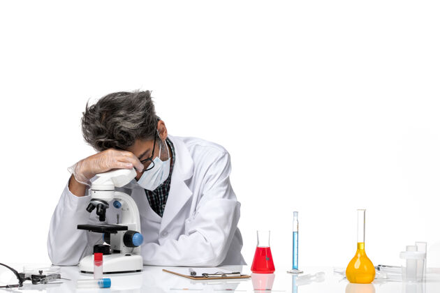 人正面图穿着白色医疗服的中年科学家坐着使用显微镜技师实验坐姿