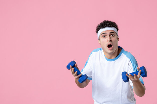运动正面图穿着运动服的年轻男性在粉色墙上用哑铃锻炼健身房人前面