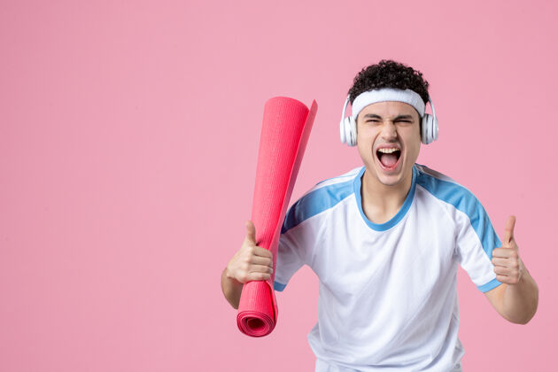 锻炼正面图穿着运动服的年轻男性 粉色墙上有瑜伽垫视图成功竖起大拇指