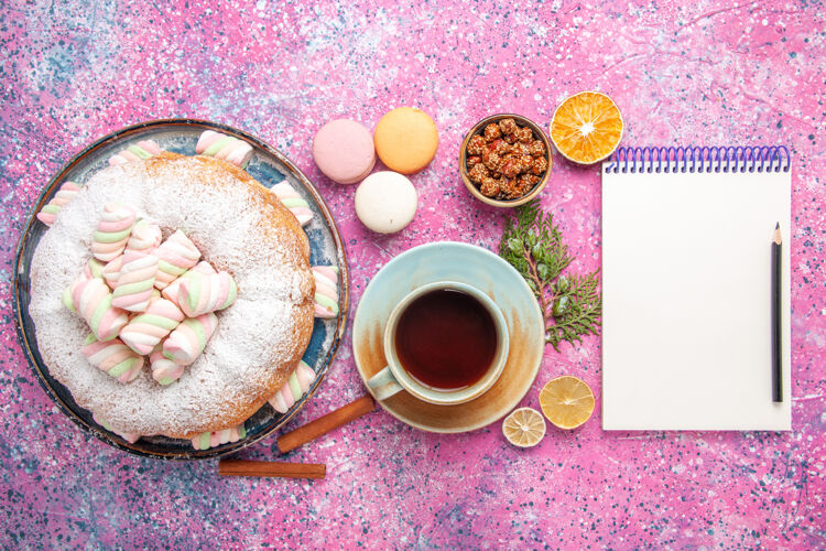 糖粉红色表面上有一杯茶和法式马卡龙的糖粉蛋糕俯视图含糖芳香咖啡