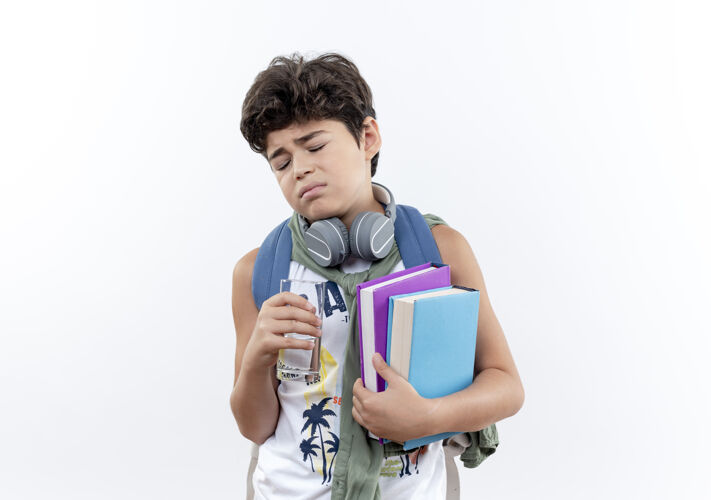 耳机闭上眼睛悲伤的小男生背着书包 戴着耳机 手里拿着一杯水和一本书 孤零零地放在白色的纸上包举行白