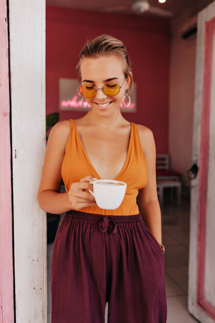 装束迷人可爱的金发女士穿着橙色t恤在夏日温暖的日子里在外面喝咖啡女人味散步诱惑