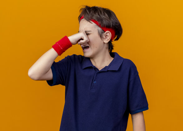 背带哭泣的年轻英俊的运动男孩戴着头带和戴着牙套的腕带擦着橘色墙上孤立的眼泪湿巾姿势脸