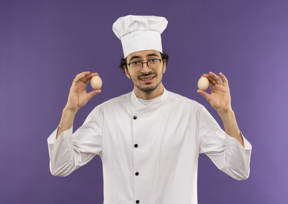 背景面带微笑的年轻男厨师穿着厨师制服 戴着眼镜 手里拿着紫色的鸡蛋制服紫色厨师