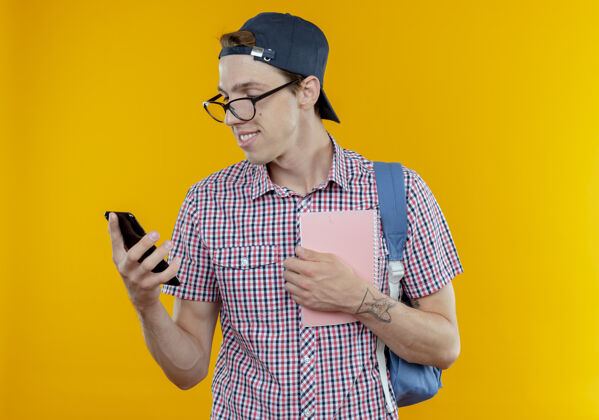 帽子高兴的小男生背着书包 戴着眼镜 戴着帽子 拿着笔记本 看着手机 手上孤零零的一片白色男孩背包